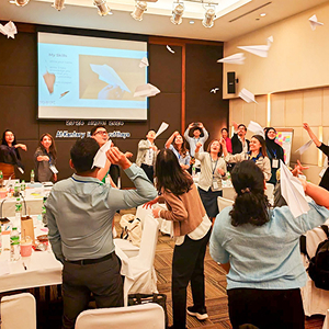 Group of diverse professionals participating in a team-building activity, enthusiastically throwing paper airplanes indoors during a conference or workshop.