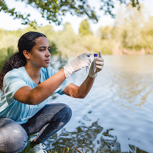 Young woman wearing gloves taking a water sample from a lake or pond for testing.